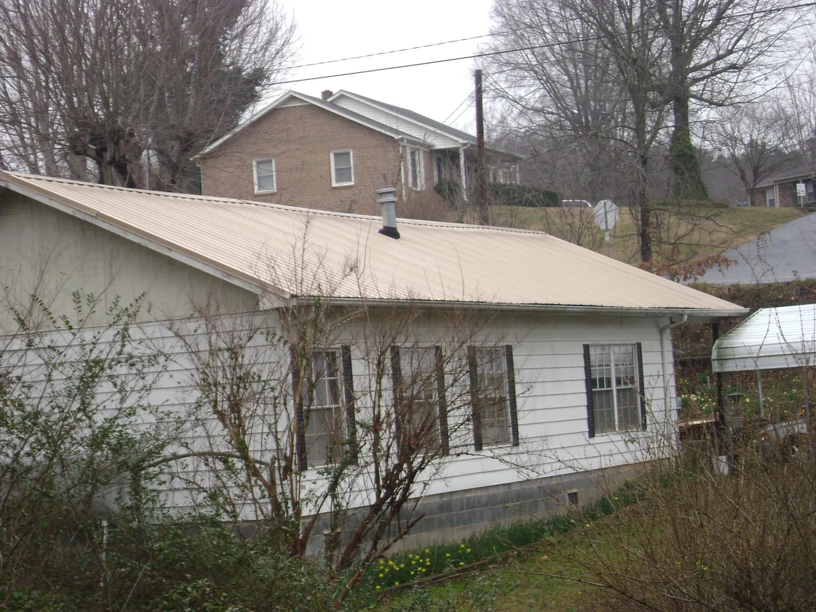 Tan metal roof on a white sided house set into a hillside — Commercial Roofing by Roofing Brothers in Danville